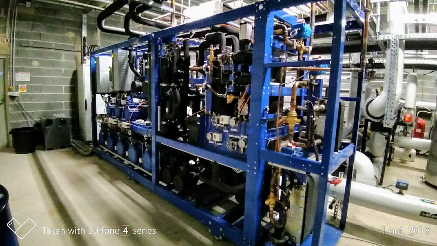 Grand ensemble machine industrielle bleu avec tuyaux et vannes, dans local technique, près d'un mur en blocs de béton.