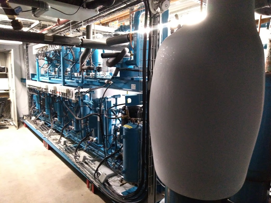 Système de refroidissement industriel bleu avec multiples compresseurs, tuyaux isolés et gros réservoir givré en premier plan.