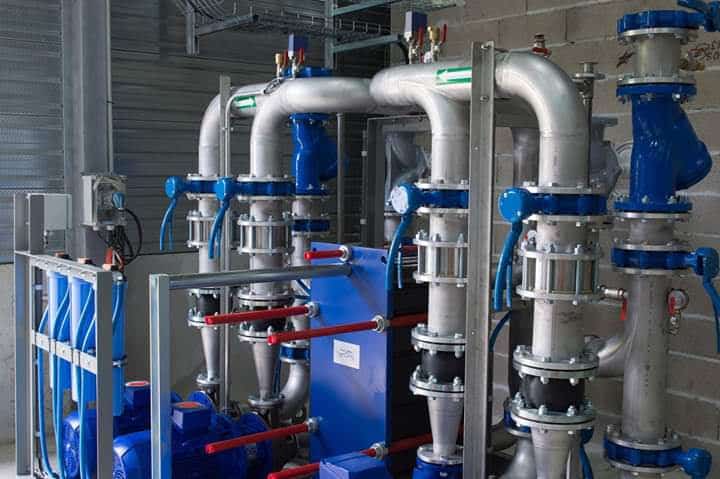 Système industriel de traitement avec tuyauterie argentée, vannes bleues, pompes et unités de filtration bleues. Flèches vertes directionnelles.