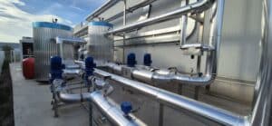 Installation industrielle extérieure avec tuyauterie isolée, réservoirs cylindriques, pompes bleues, moteurs et jauges. Système de refroidissement moderne.